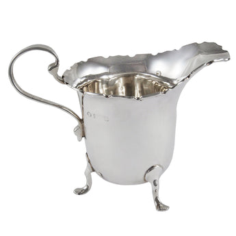 An early 20th century, silver cream jug with a scalloped rim on three feet.
