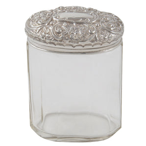 An Edwardian, faceted glass jar with an embossed silver lid & vacant cartouche.