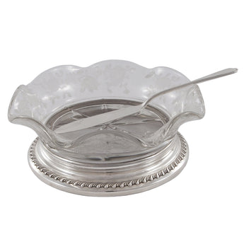 A silver butter dish with a glass bowl featuring a floral pattern & frill edge with a silver butter knife.