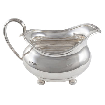 An early 20th century, silver cream jug on four ball feet.