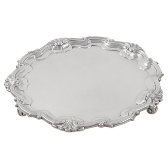 An Edwardian, silver, circular salver with raised shell & scroll border on three scroll feet.