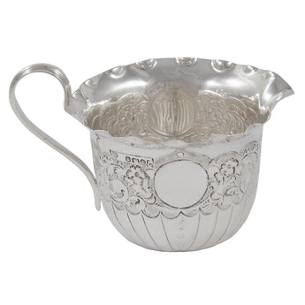 A Victorian, silver cream jug with an embossed floral & foliate design & a vacant cartouche.