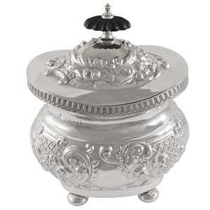 An Edwardian, silver tea caddy with foliate & scroll decoration, a fluted border, ebonised finial & four ball feet.