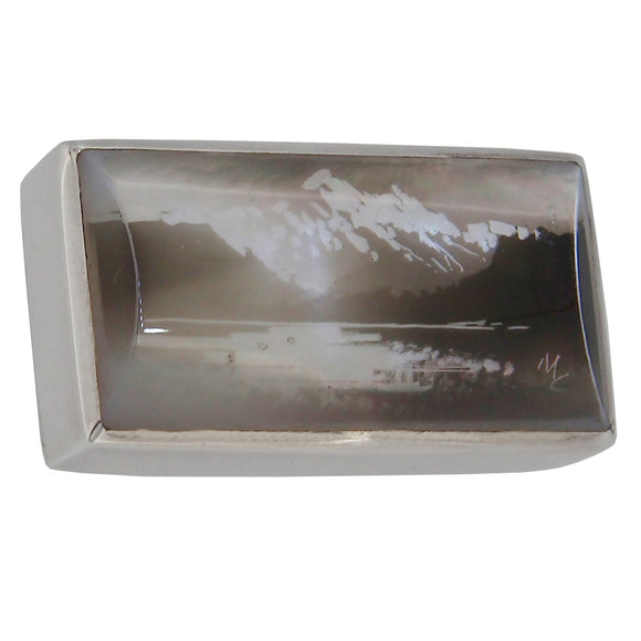 A modern, silver, rectangular, candle smoked brooch, featuring an image of a lake & mountains
