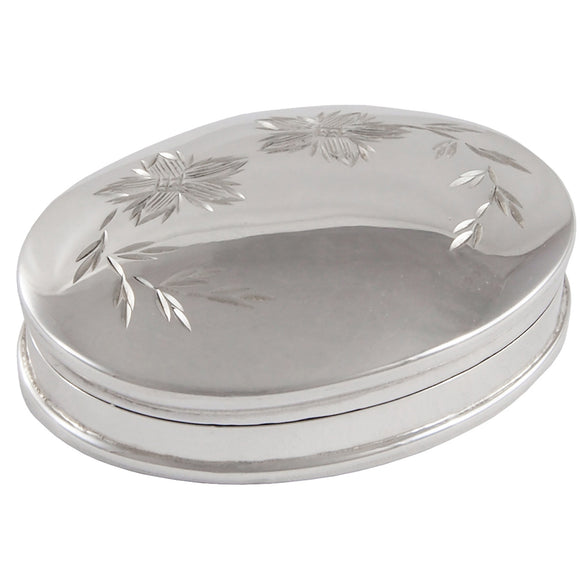 A modern, silver, oval pill box with a diamond cut floral pattern on the lid