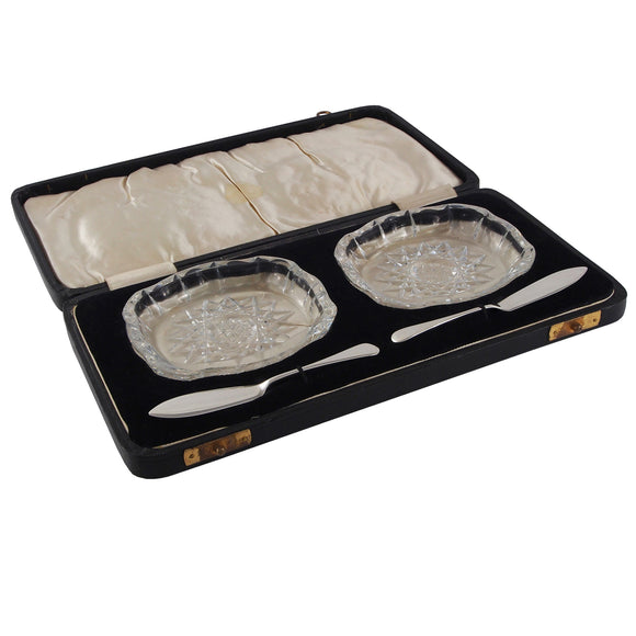 A pair of early 20th century, cut glass butter dishes & silver butter knives & fitted case.