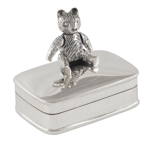 A modern, silver, rectangular box with a teddy bear seated on the lid.