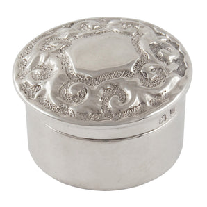 A Victorian, silver, circular lidded pot with an embossed scroll & foliate decoration & a vacant cartouche.